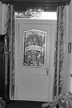 Lübecker Straße (2): Bauernhof: Wohnhaus: Innenansicht: Flur: Eingangstür mit Glasscheibe, Oberlicht, mit Glasschliff und Ätzung, florale Motive, Namenszug Wilhelm Stapelfeld [spiegelverkehrt]: links Standuhr