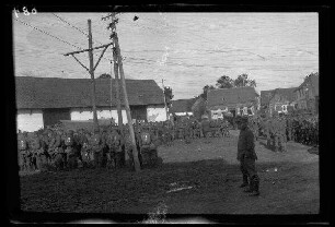 Metz-en-Couture (Dep. Pas-de-Calais, Frankreich): Appell von Soldaten mit Marschgepäck auf einem Platz vor einem landwirtschaftlichen Gebäude, im Hintergrund Wohnhäuser (Distanzaufnahme)