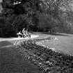 Schlosspark: Parkweg mit Parkbänken: auf einer Bank Frauen, mit Kindern, Kinderwagen: Bäume: auf Rasen geschwungene Blumenrabatte