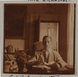 Rudolf Borchardt sitzt mit Buch am Schreibtisch