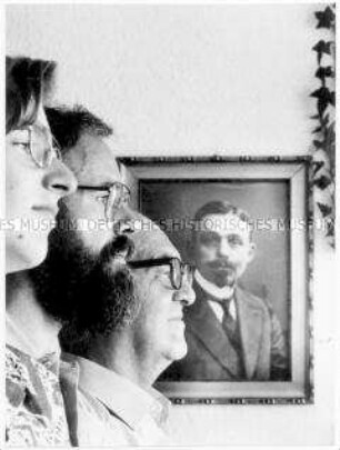 Drei hintereinander stehende Männer unterschiedlichen Alters im Profil, im Hintergrund Gemälde eines männlichen Vorfahren (Prämiertes Foto Sonderthema: Familienbilder)