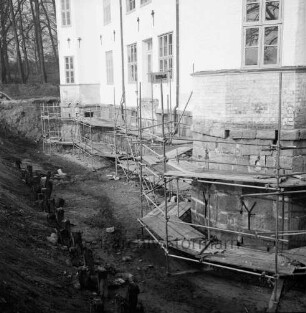 Restaurierung: innerer Graben ausgehoben: Pfosten der früheren Grabenversteifung mit Holzbohlen am Grabenfuß: Gerüst an Schlossfundament