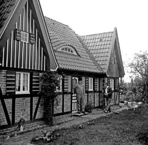 Siebenbäumen (Kreis Herzogtum Lauenburg): Siebenbäumener Mühle: Restaurierung: restauriertes und wiederaufgebautes Fachwerkhaus des Gutes Trenthorst: davor zwei Männer und Hund: vorn Rasenfläche: hinten rechts Büsche