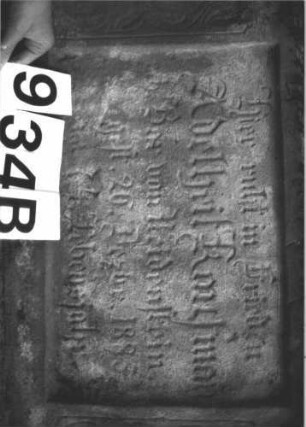 Grabstein 934 (Index: 99899437) Material: Sandstein, Marmortafel Zustand: Sandstein stark verwittert, Marmortafel gut erhalten Maße HxBxT: 179x55x19 cm Beschreibung: aufgesockelte Stele mit Dreiecksabschluss, oben hochrechteckig erhöht, Eckakroterien, im Dreiecksfeld Ranken, eingelassene Inschrifttafel durch Säulen mit Schilfkapitellen gerahmt Symbolik: Ranken: Grabstein 934B