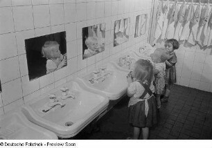 Drei Kleinkinder an Waschbecken eines Kinderkrippenbaderaums beim Zähneputzen