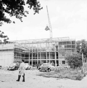Rathaus und Bürgerhaus Glinde [später Marcellin-Verbe-Haus]: Richtfest: Hochziehen der Richtkrone mit Baukran: vor dem Bau Gäste und drei VW-Käfer: vorn links Mann