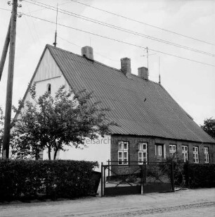 Bauernhaus mit Vorgarten und Hecke: ehemalige Volksschule: links Baum und Strommast