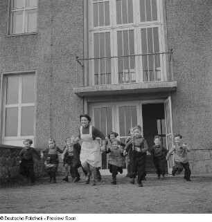 Kindergärtnerin mit Kindern vor dem Kindergartengebäude