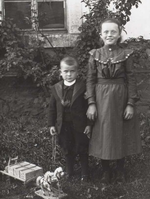 Mädchen und kleiner Junge mit Spielzeugpferd und -wagen