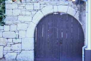 Kalksteinmauer und steinerner Torbogen in der Kirchhofsmauer, Holztor