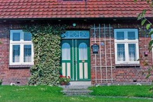 Oetjendorf: Oetjendorfer Landstraße 57: traufständiges Wohnhaus aus Backstein: Straßenfront, Teilansicht: Eingangstür mit Oberlicht, Rankgitter, Kletterpflanze, Fenster