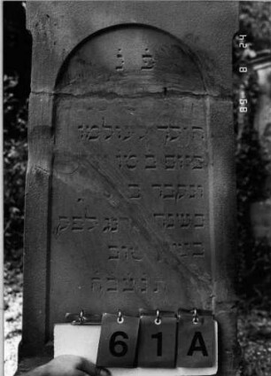Grabstein 61 (Index: 100086513) Material: Sandstein Zustand: gebrochenen und repariert mit Textverlust Maße HxBxT: 150x54x16 cm Beschreibung: Stele, getreppter Sockel, giebelartiger Abschluß mit Verdachung und Eckakroteren, eingetieftes Schriftfeld mit Rundbogen: Grabstein 61A