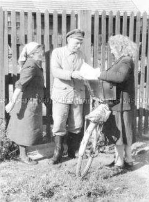 Briefträgerin übergibt Post an einen Genossenschaftsbauern der LPG Löwenberg (Kr. Gransee) sowie seine Frau