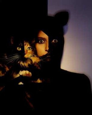 Delia mit Katze DIA : Model in schwarzem Kleid mit Kopfschmuck in Katzenform mit Katze auf Arm
