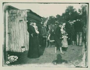 Frau mit Kleinkind auf dem Arm vor einer Latrine