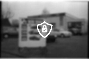 Autohaus [Name maskiert] Gänseberg: Außenansicht mit Firmenname: davor Parkplatz, Pkws zum Verkauf, Werbeschild Peugeot: 21. Februar 1990