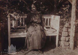 Auf einer Gartenbank im Schatten eines Baumes sitzende Frau