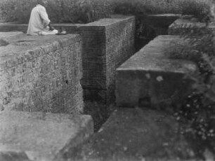 Steinwände mit Ornamenten : Steinwände, die mit Ornamenten verziert sind. Auf einer Steinmauer sitzt ein Mann.