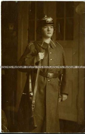 Frau mit Pickelhaube, Militärmantel und Gewehr