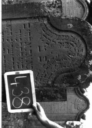 Grabstein 438 (Index: 100102746) Material: Sandstein Zustand: an den Rändern leicht verwittert Maße HxBxT: 120x62x9 cm Beschreibung: Stele, eingezogener Rundbogenabschluss, Schriftfeld eingetieft mit stark überhöhtem Konvexbogenabschluss: Grabstein 438 (Detailaufnahme)
