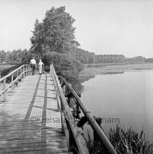 Herrenteich: Fischhuser Damm: hölzerne Fußgängerbrücke: Mann, Junge mit Stöcken auf Brücke: Blick Richtung Norden
