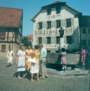 Bad Kissingen. Darstellung eines Festumzuges an einer Hauswand, davor der Minnesängerbrunnen
