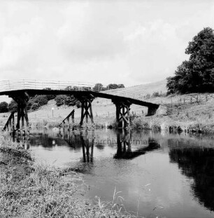 Klein Barnitz: Holzbrücke für Fußgänger über Trave: hinten Wiesen mit Zaun und Bäume