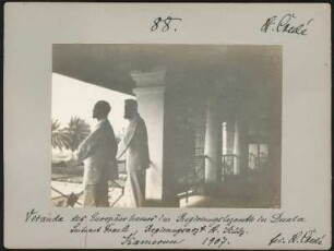 Portrait von Leutnant Frank und Regierungsarzt Dr. Külz im Regierungskrankenhaus von Douala : Seitliche Rückansicht von zwei Männern, am Geländer des Arkadengangs des sogenannten "Europäerhauses"stehend