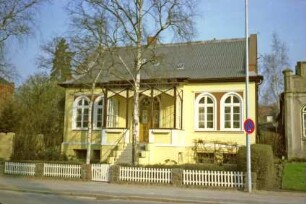 Lübecker Straße 39: traufständiges Wohnhaus: Straßenfront mit Rundbogenfenstern, Eingangsveranda, Treppe und Eingangstür: davor Vorgarten, zwei Birkenbäume, Lattenzaun