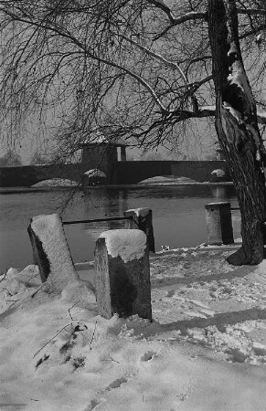 Parklandschaft im Winter mit Wasserlauf und Brücke