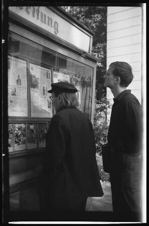 Männer vor dem Schaukasten der "National Zeitung" mit einem Bericht über die Vorbereitungen zur EM im Schwimmen 1934 in Magdeburg