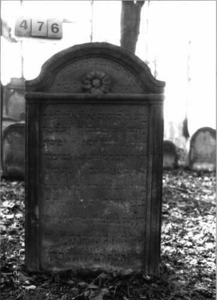 Grabstein 476 (Index: 100115529) Material: Sandstein Zustand: verwittert mit Textverlust Maße HxBxT: 60x42x9 cm Beschreibung: Stele mit eingezogenem Segmentbogenabschluß, eingetieftes, zweigeteiltes Schriftfeld Symbolik: Blüte: Grabstein 476