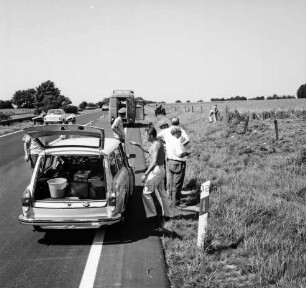 Mord an Brigitte Wetzenstein-Ollenschläger: Bundesautobahn A 1 bei Reinfeld: Leichenfundort im Graben neben Seitenstreifen am 19. August 1972: vorn links am Straßenrand Polizisten an Pkw mit geöffneter Heckklappe: dahinter Polizeifahrzeug: hinten links Autobahn mit Pkws: hinten Mitte wegfahrender Trecker nach Mähen eines Teils des Grases und des angrenzenden Getreidefeldes: rechts daneben Mann am Zaun: hinten Bäume