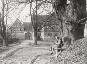 Syhra. Gehöft (1801/1850). Straßenansicht mit lesender Frau auf einer Bank an mächtiger Linde