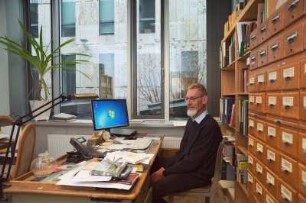 Porträt Perk Loesch, Fachreferent der SLUB : Porträt des Kunstwissenschaftlers Perk Loesch, Fachreferent und von 1996 bis 2019 Leiter der Handschriftenabteilung an der Sächsischen Landesbibliothek – Staats- und Universitätsbibliothek Dresden (SLUB). Aufnahme an seinem Schreibtisch