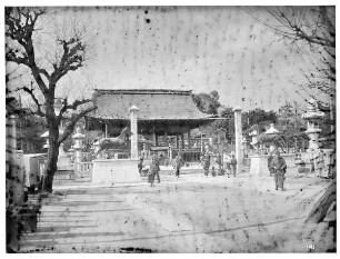Kobe, Japan. Nanko Tempel. Einheimische vor der Eingangshalle mit flankierenden Pferdestatuen (nach 1910) an den Inschriftpfeilern