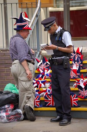 Kontrolle : Der Mann, der britische Hüte anbietet, wird von einem Polizisten am Tower notiert, weil er offenbar seinen Verkaufsstand illegal betreibt. Aufgenommen im Mai 2006. Foto Uwe Gerig