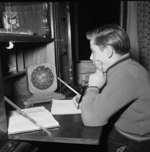 Junger Mann im Profil nach links, an Schreibtisch vor astrologischer Uhr sitzend