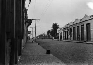 Straßenszene : Straße in Parajuí mit Gebäuden und Bürgersteigen rechts und links der gepflasterten Straße. Auf der linken Seite Masten mit Leitungen.