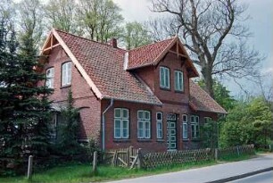 Allee 1: traufständiges Wohnhaus aus Backstein: Straßenfront mit Sprossenfenstern, Eingangstür, darüber Zwerchhaus nach Erneuerung von Ortgängen und Giebelzier aus Holz: Giebelseite mit Wintergarten [halb verdeckt]: davor Jägerzaun: 5. Mai 1994