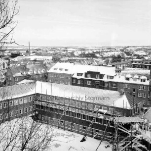 Erweiterungsbau mit Kreistagssitzungssaal [später Gebäude C]: IV. Bauabschnitt: Gebäude mit gedecktem Dach und Gerüst: vorn rechts Kreistagssitzungssaal: Blick vom Erweiterungsbau "Hochhaus" [später Gebäude B]: dahinter Wohnblocks an der Reimer-Hansen-Straße und der Mewesstraße: Winter