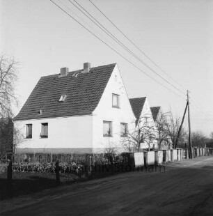 Neubausiedlung: Einfamilienhäuser mit Vorgärten hinter Zäunen: davor Strommasten