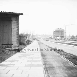 Hamburger Straße / Lorentzenstraße: vorn asphaltierte Straße und gepflasterter Fußweg: rechts Gebäude: hinten Baubude, Erdhaufen, Baumaterial und Bagger: hinten rechts Hochhaus mit Gerüst und Pkws: hinten Mitte Wohnhäuser und Tankstelle
