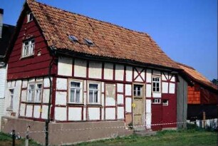 kleines Fachwerkhaus mit ziegelbehangenem Giebel; daran kleines Wirtschaftsgebäude
