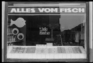 Schaufenster eines Fischgeschäfts mit Aufschriften "Alles vom Fisch" und "4 Sorten Ölsardinen"
