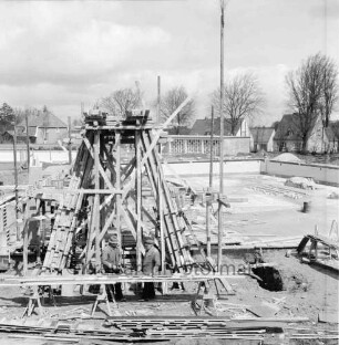 Freibad: Reeshoop: Schwimmbecken in Bau, mit Fliesen: Sprungturm in Bau, Gerüst: zwei Handwerker an Werkbank: hinten Zaun: hinten Mitte Filterhaus: hinten links Nichtschwimmerbecken: im Hintergrung Wohnhäuser am Reeshoop