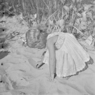 Kleines Mädchen mit Kleid spielt am Strand