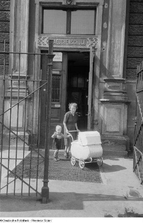 Eine Frau mit Kind und Kinderwagen vor einem Schulgebäude