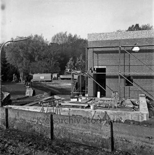Zentralklärwerk: Anna-Heitmann-Weg: Erweiterung der Schlammaufbereitungsanlage: Gebäude mit Gerüst: Betonmauer, Schubkarre, Baustahlmatten: Verschalung: Baumaterialien: hinten Baufahrzeuge, Arbeiter, Transportband