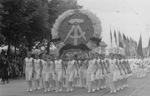 Sportler tragen auf einer Parade anlässlich des II. Deutschen Turn- und Sportfestes das Staatswappen der DDR als monumentales Blumengesteck
